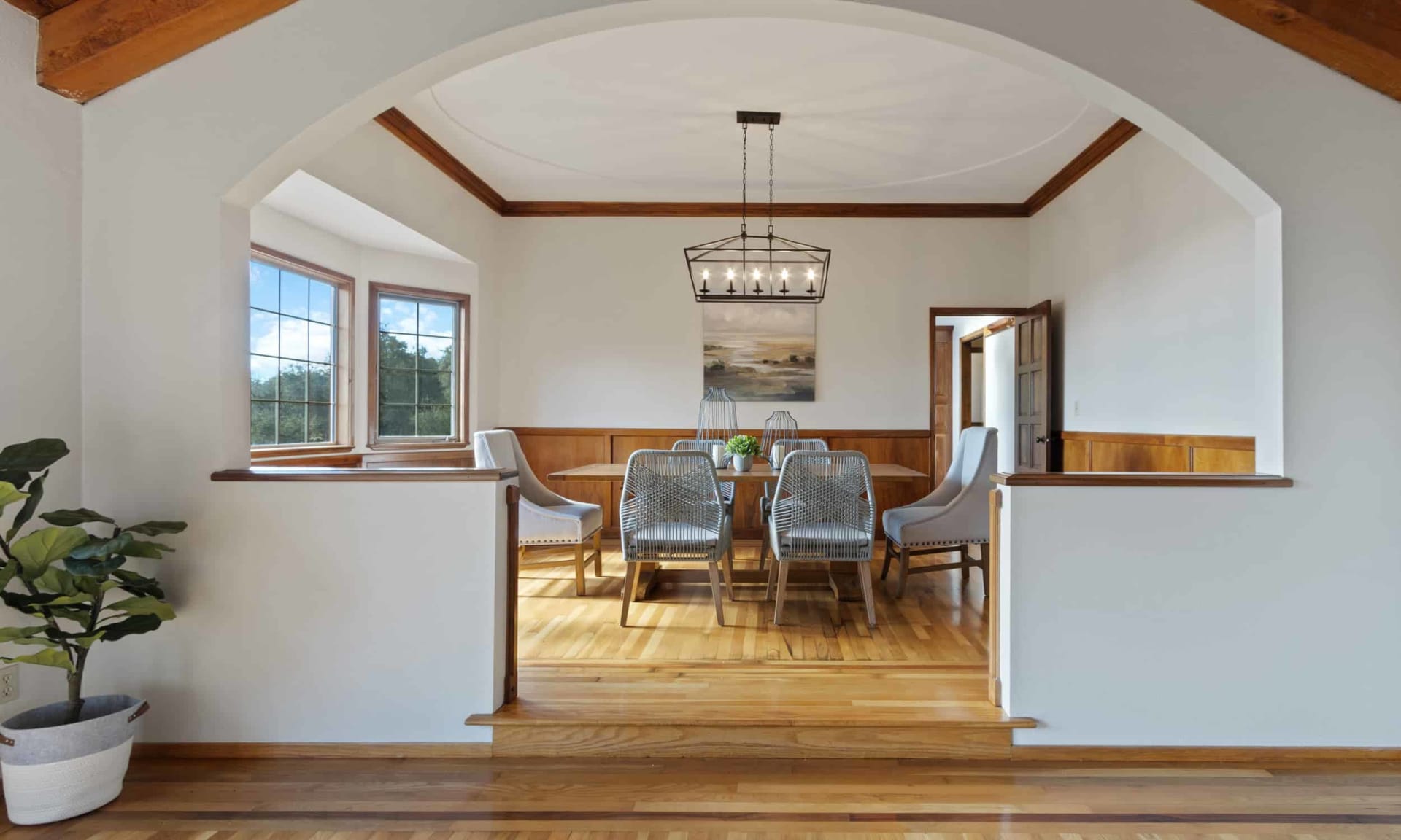 Dining room with a broad archway, wood wainscoting, tall windows, and a rectangular chandelier.