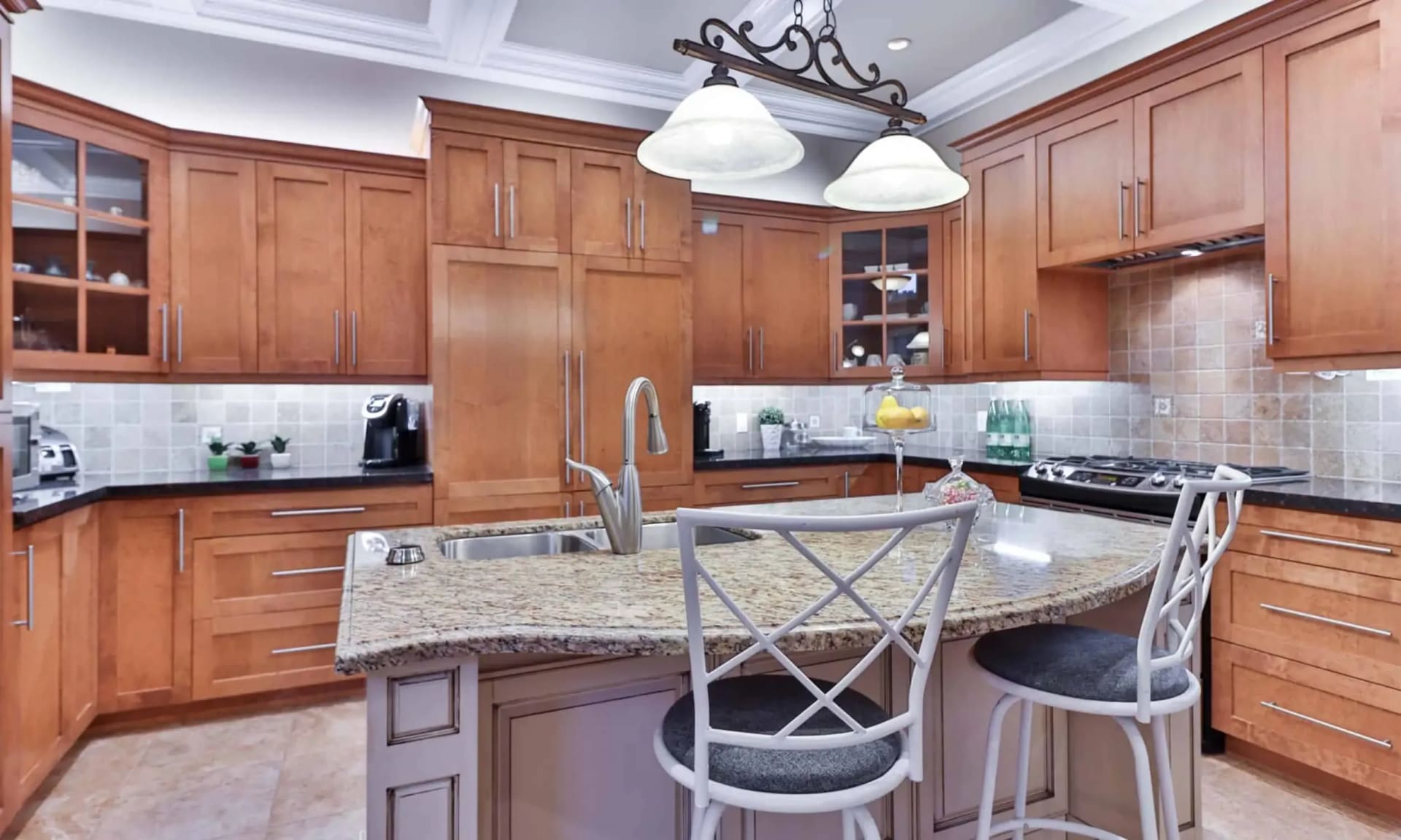 Kitchen with warm wood cabinetry, a large granite island, and pendant lights.