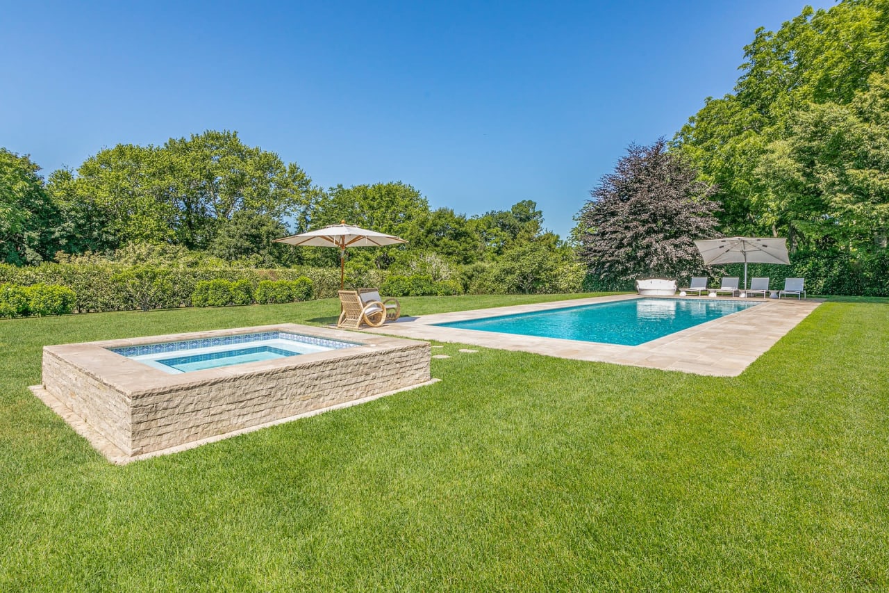 Well-maintained lawn with trees, a rectangular blue-lined pool, and a wooden hot tub with a lounge chair and table nearby.