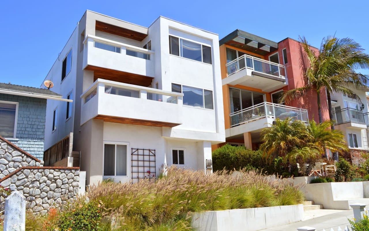 Three-story modern beach houses with balconies, surrounded by palm trees and lush greenery.