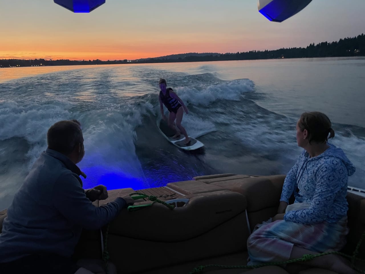 woman riding on a waveboard next to a yatch with two people watching