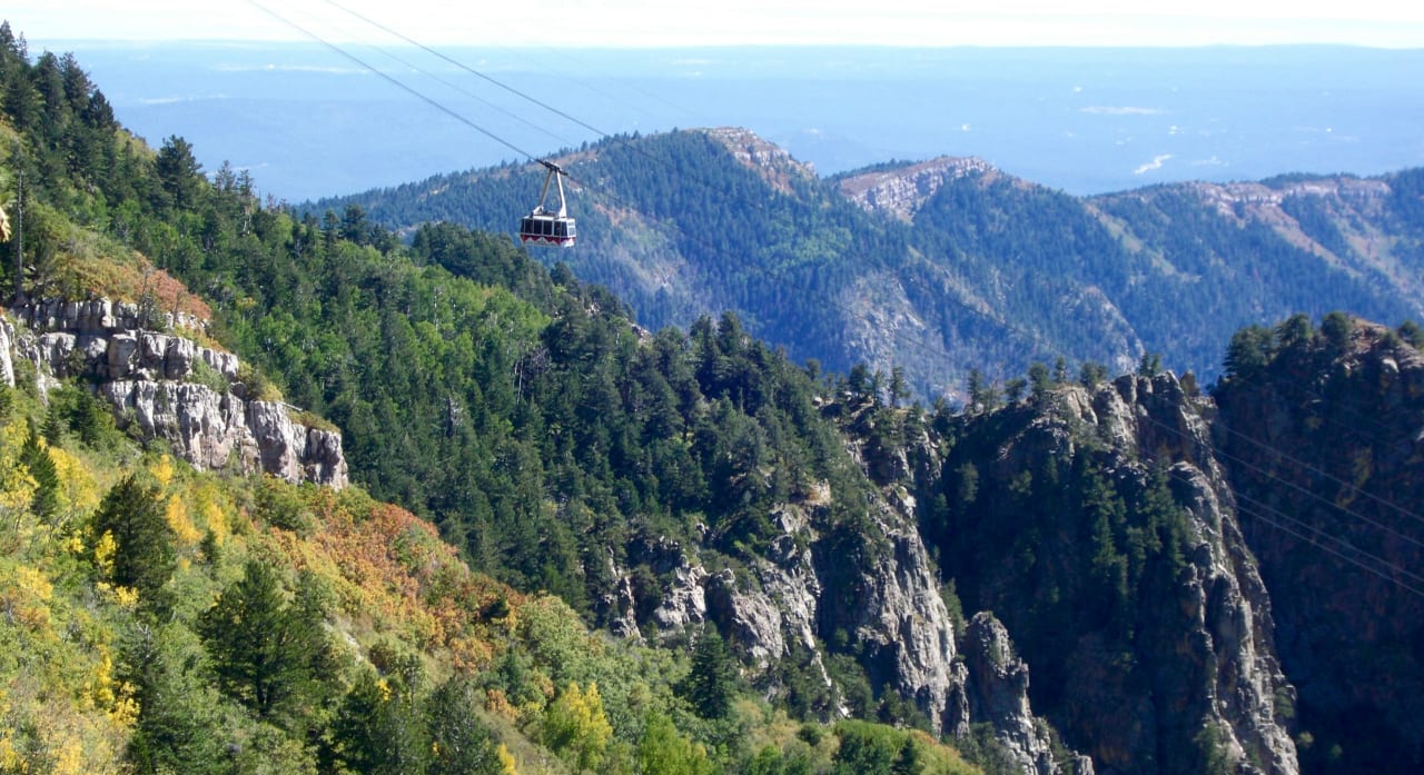 Sandia Peak Tramway car suspended over a lush green mountainous landscape.