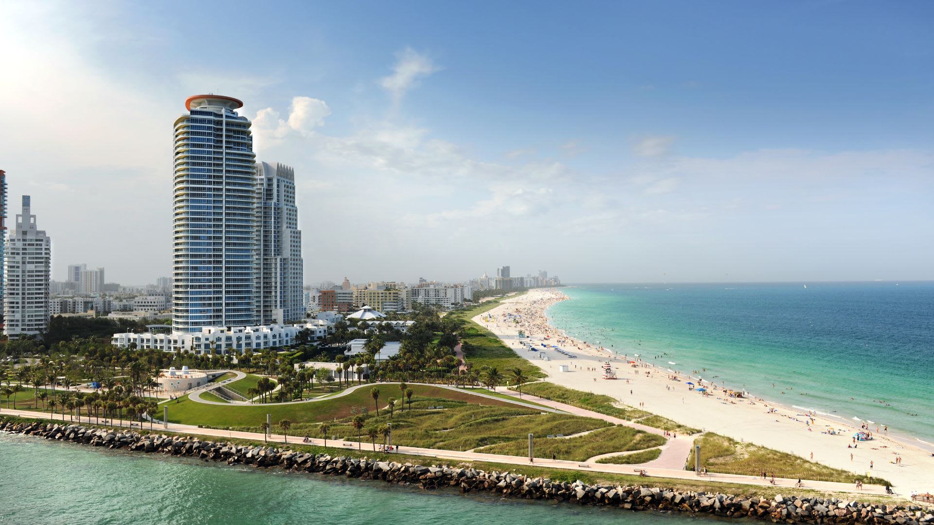 South Florida beachfront with high-rise buildings, a long sandy beach, and turquoise ocean.