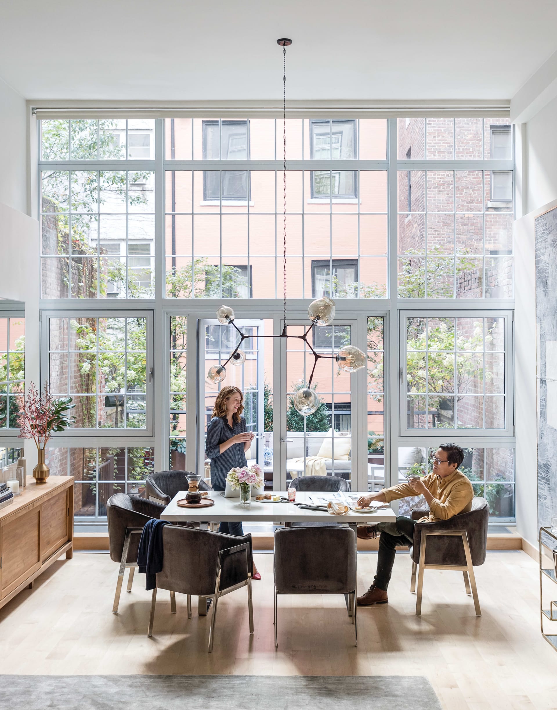 Furnished dining room with a white table, sculptural pendant light, and dramatic floor-to-ceiling windows.