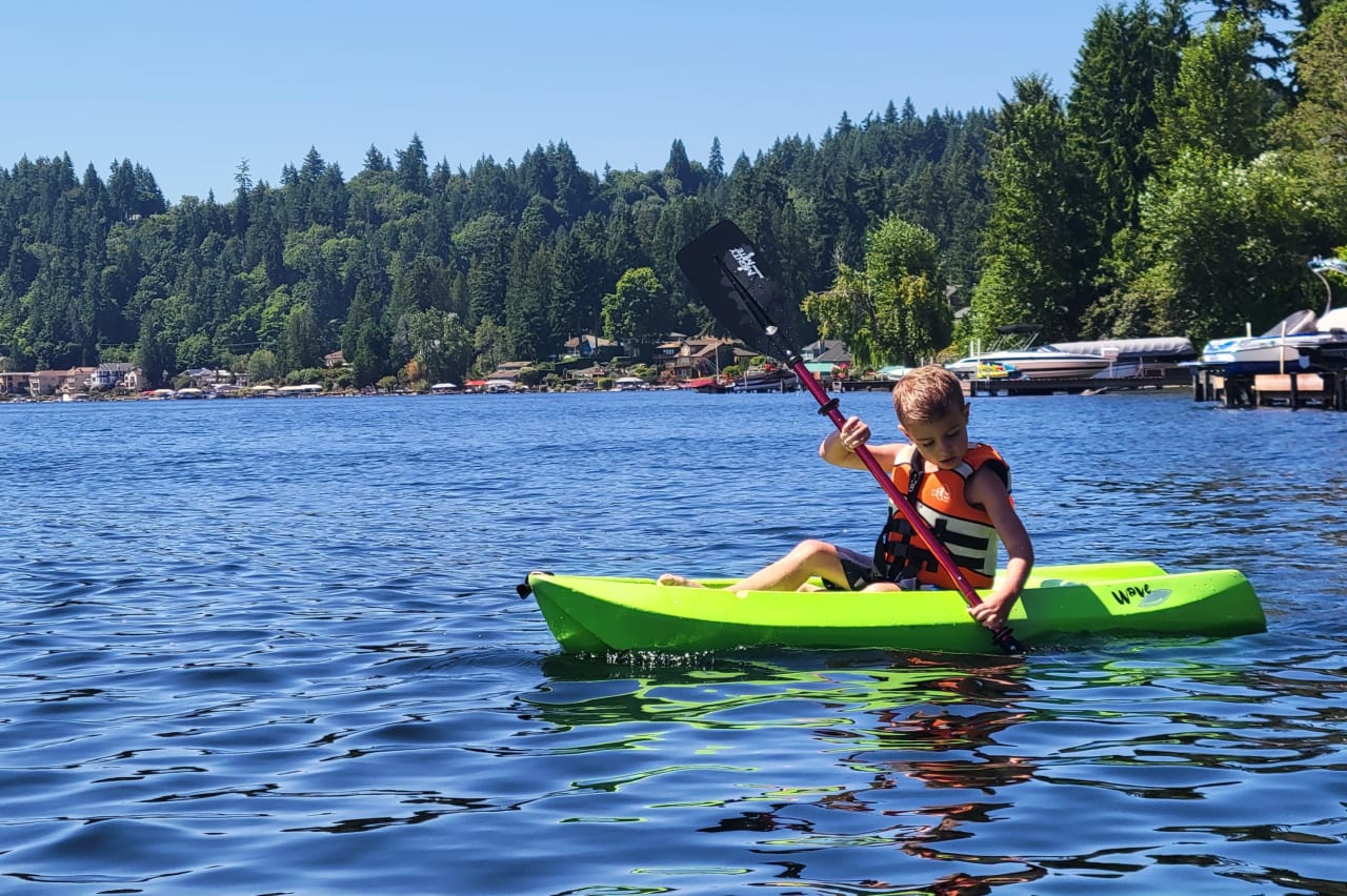 a boy paddling on a green kayak in a lake