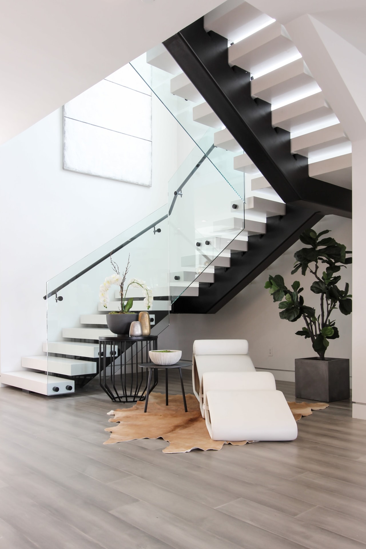 A modern, floating staircase with a glass railing winds up to a second floor.