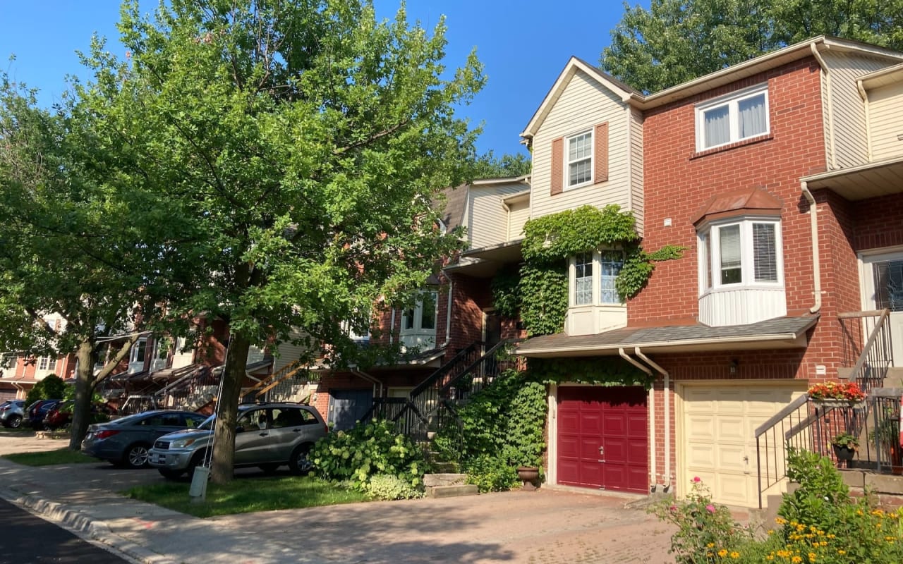 A row of four houses with cars parked in front of them.