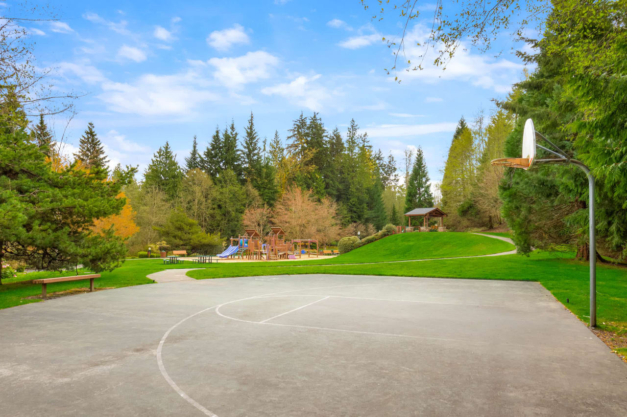 An outdoor basketball court with a playground and trees in the background