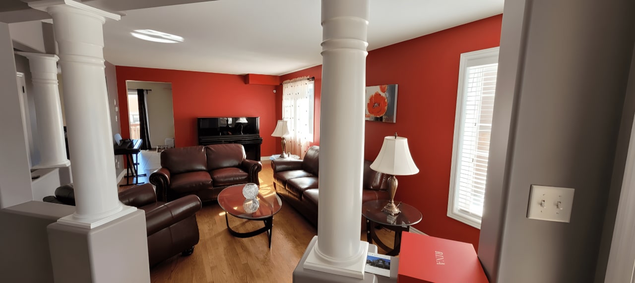 A living room with red walls, white columns, a couch, and two chairs.