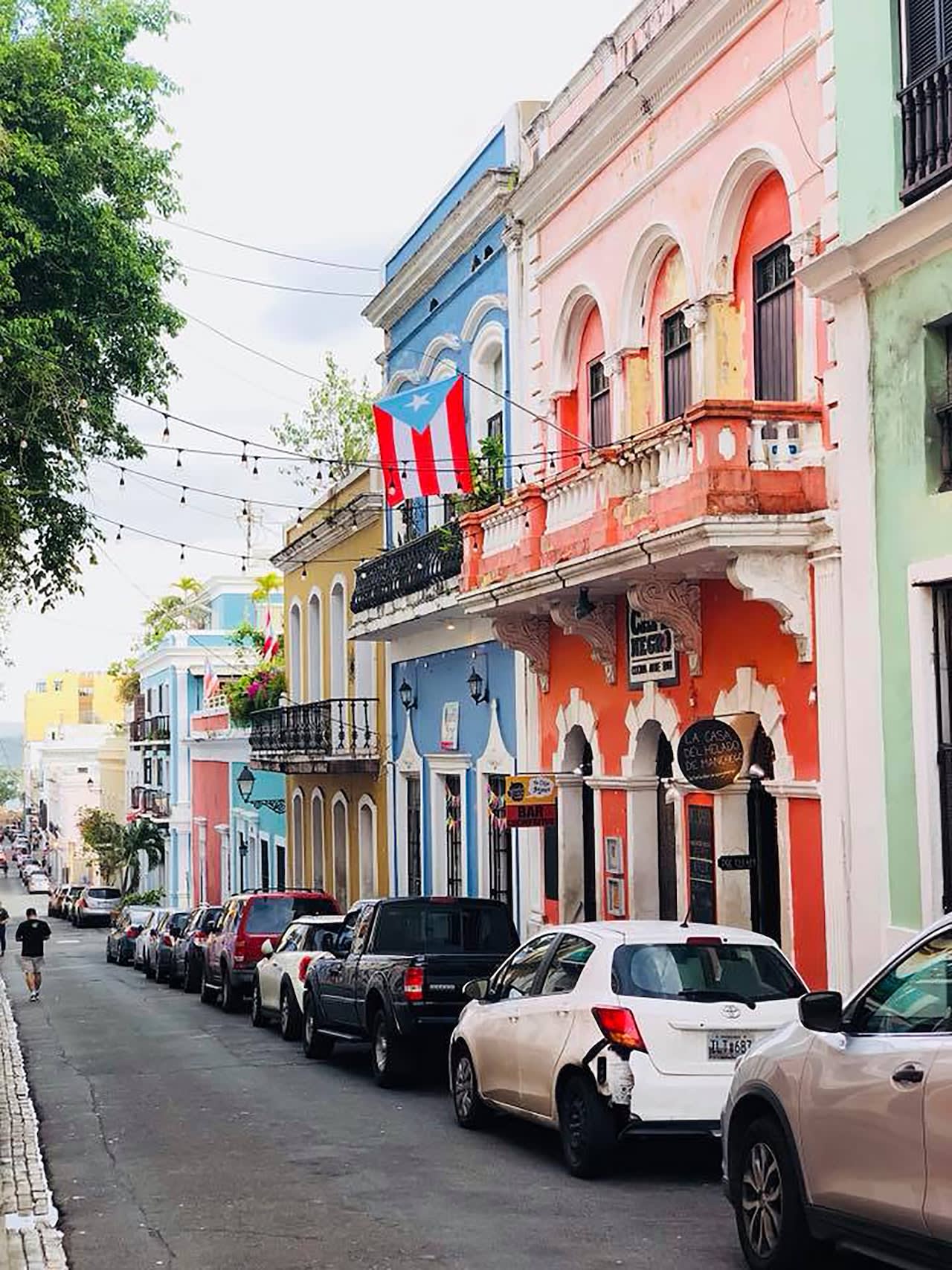 Street view of colorful colonial buildings with a Puerto Rican flag hanging from a balcony.