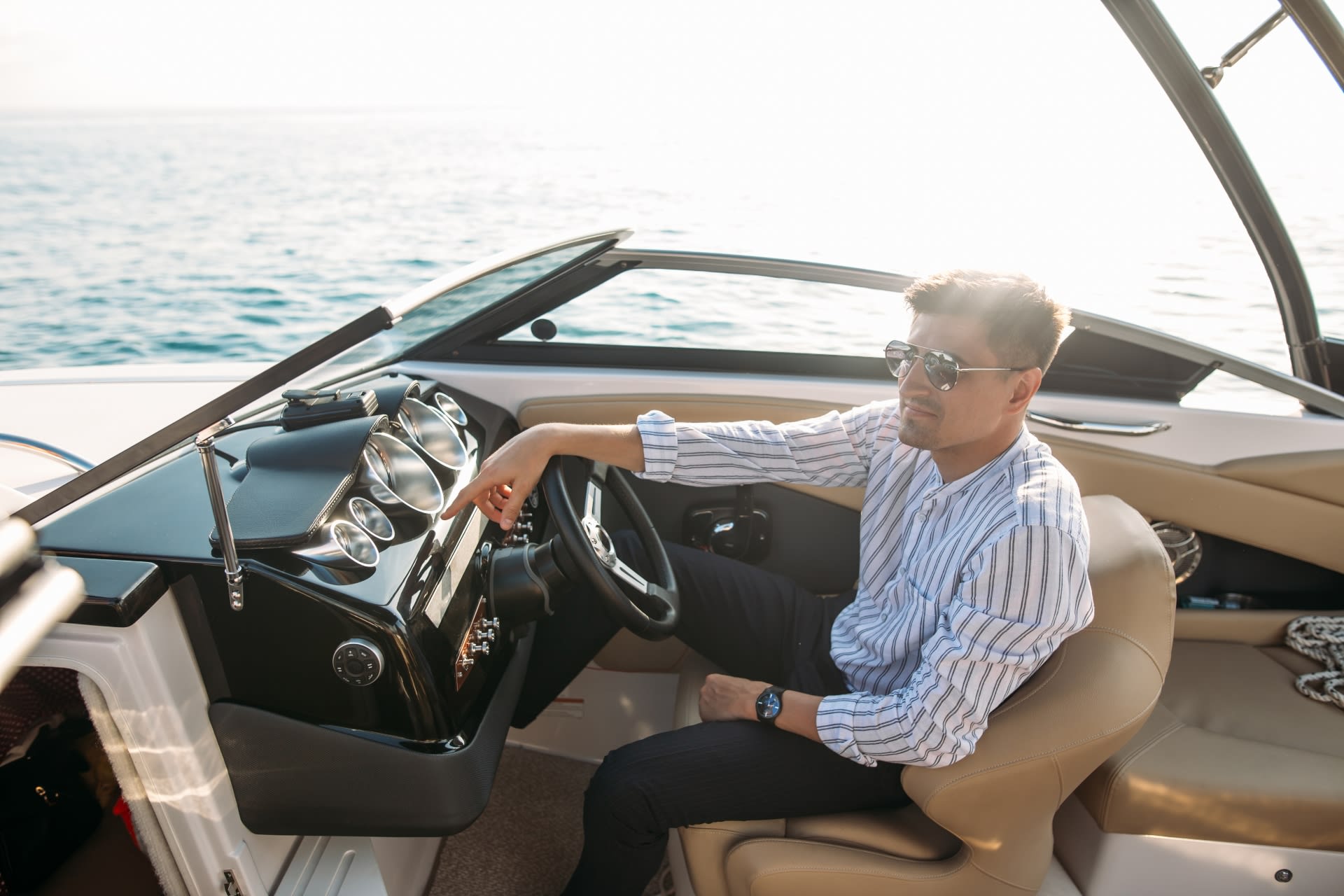 Man in sunglasses seated at a motorboat’s helm on open water in bright sunlight.