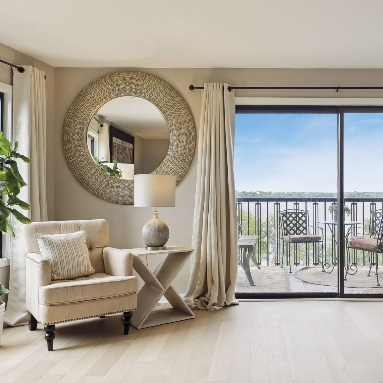 A room with a chair, a wooden coffee table, and a large mirror mounted on the wall beside the balcony.