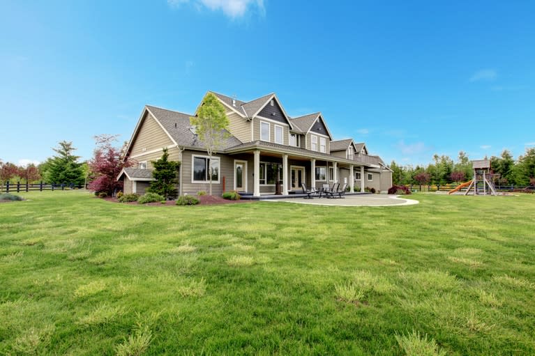 A large house with a gray roof and a big green lawn all around it.