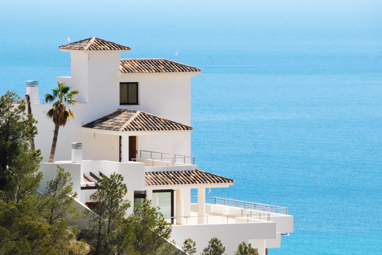 A white house with a red roof sits on top of a hill overlooking the ocean