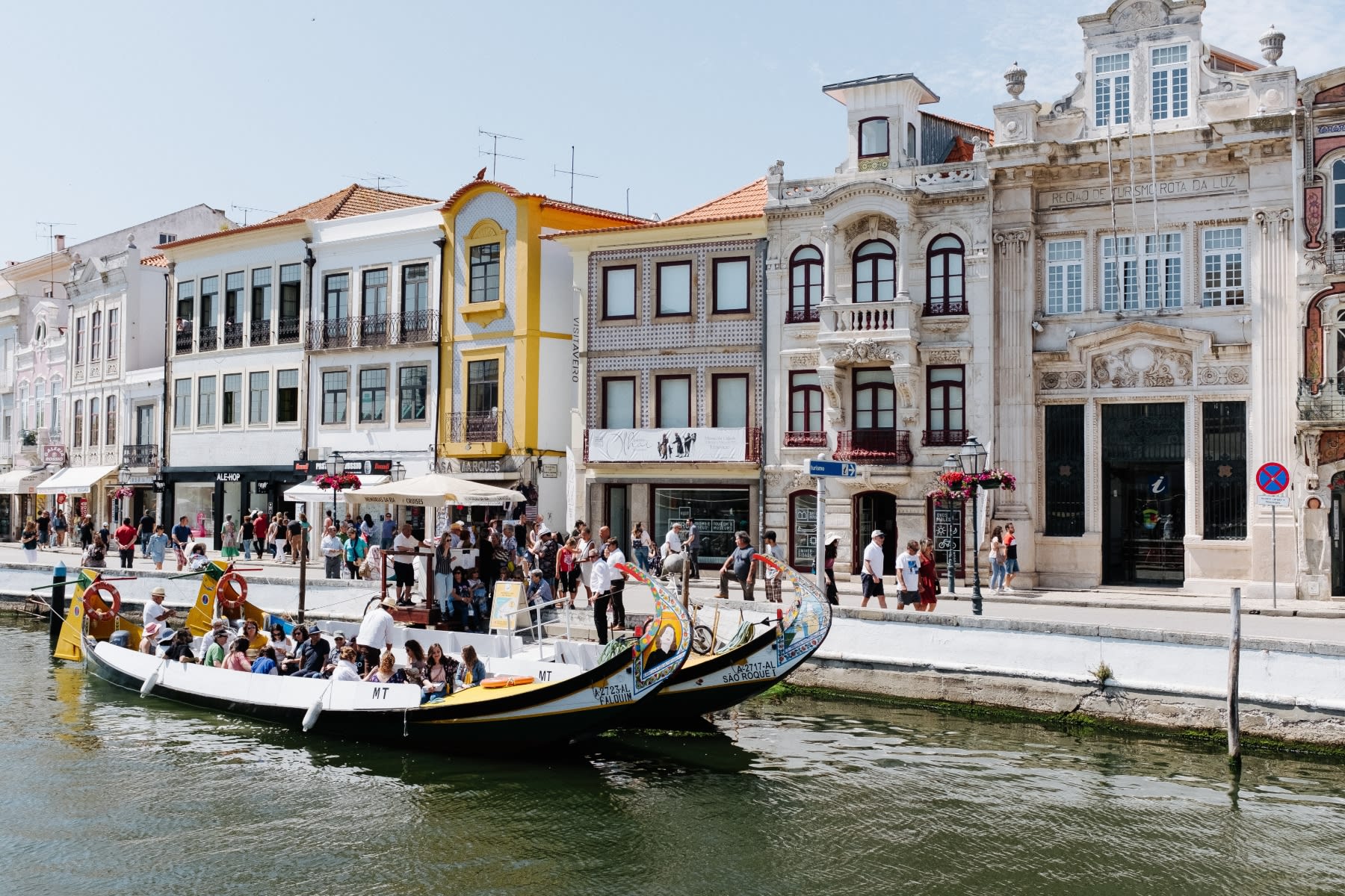 Colorful passenger boats pass ornate historic buildings along a busy canal in Portugal.