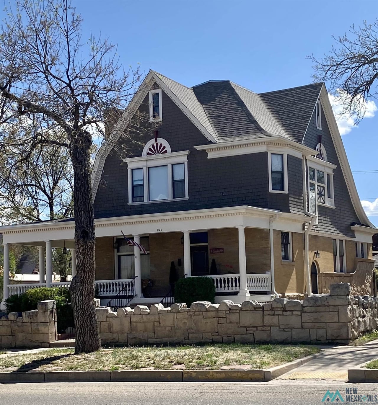 A black historical house with a stone fence in front.