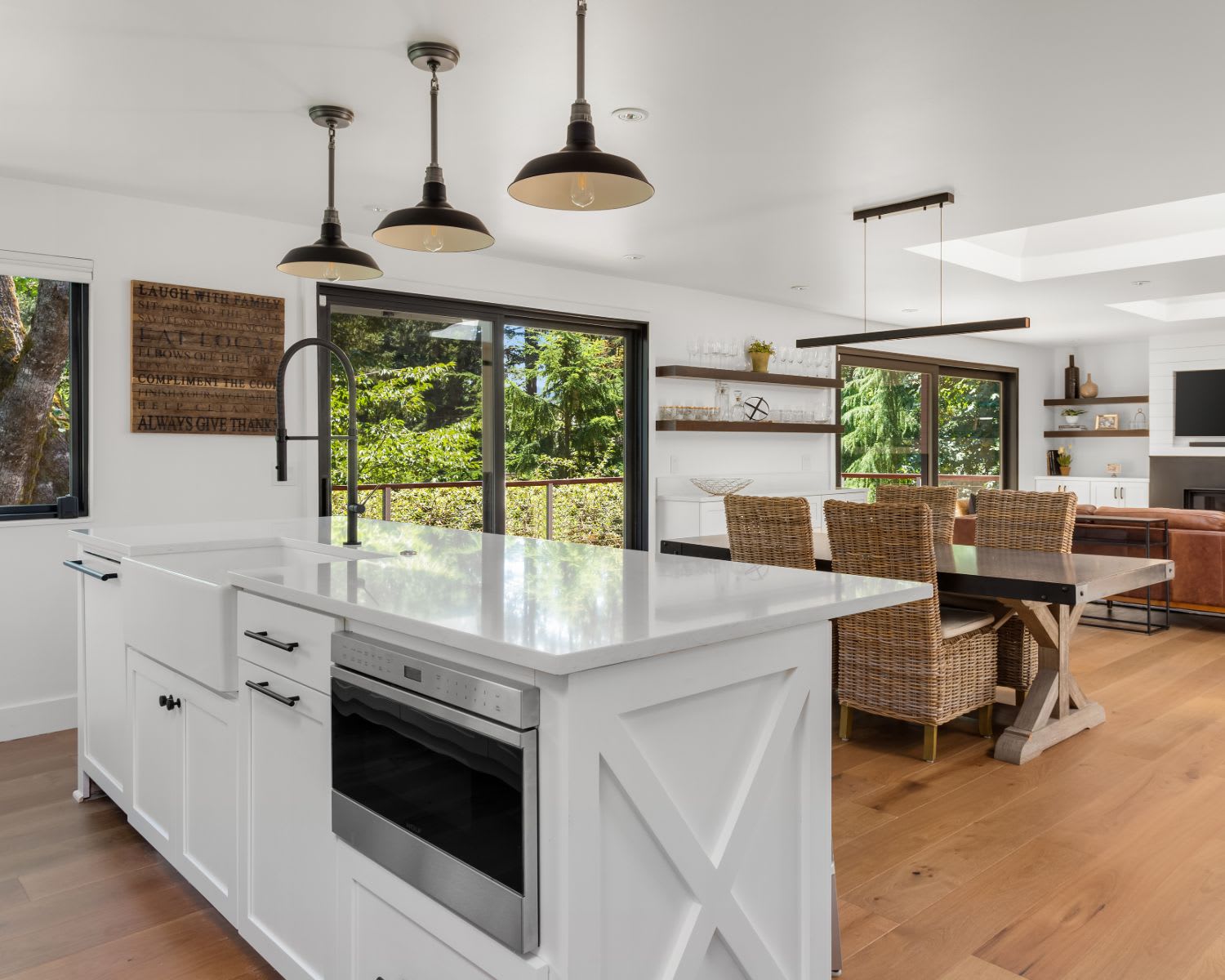 A spacious, modern kitchen with a large white island featuring a sink, a microwave drawer, and dark pendant lights hanging above. 