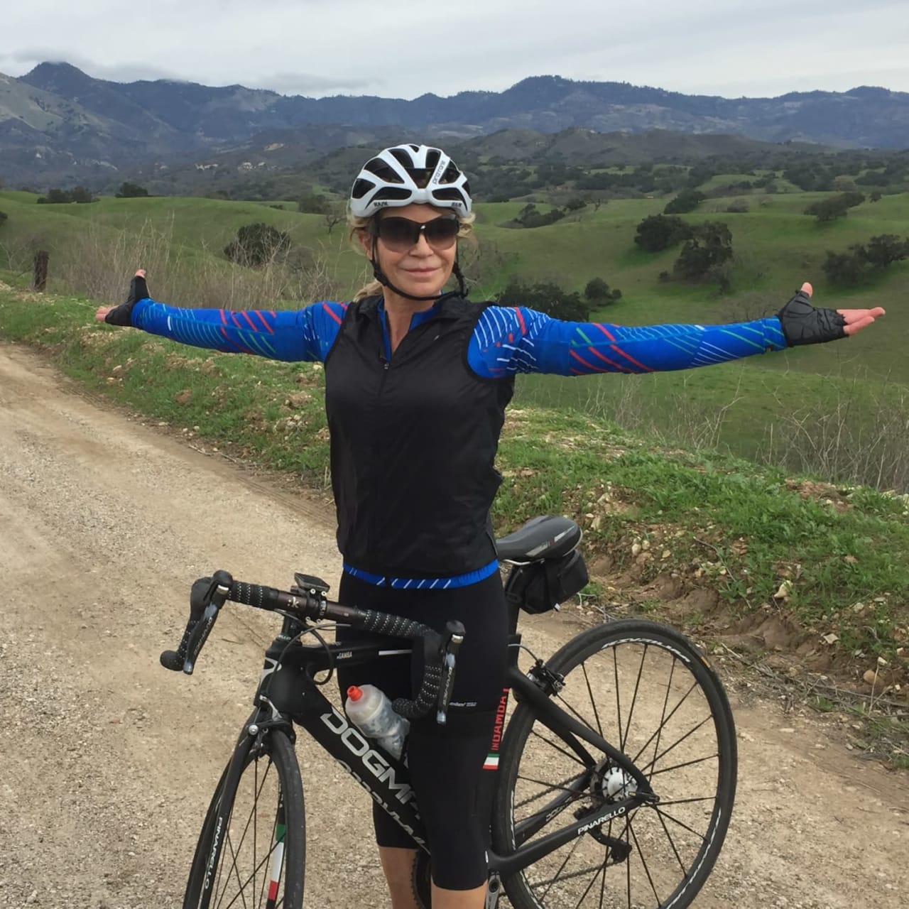 Tracy Curtis riding her mountain bike on the dirt path in the middle of green hills.