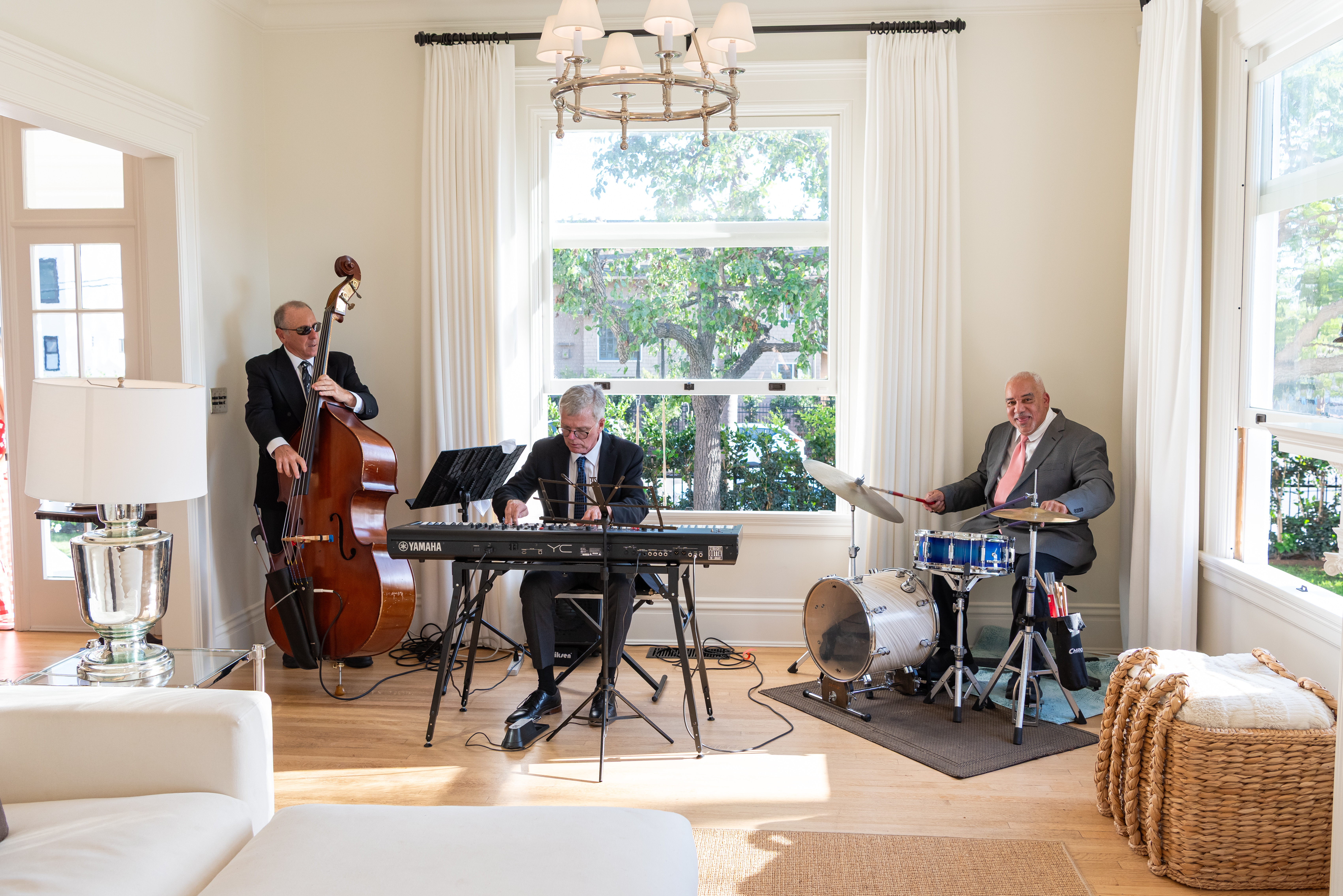 Live jazz trio with upright bass, piano, and drums playing in the living room