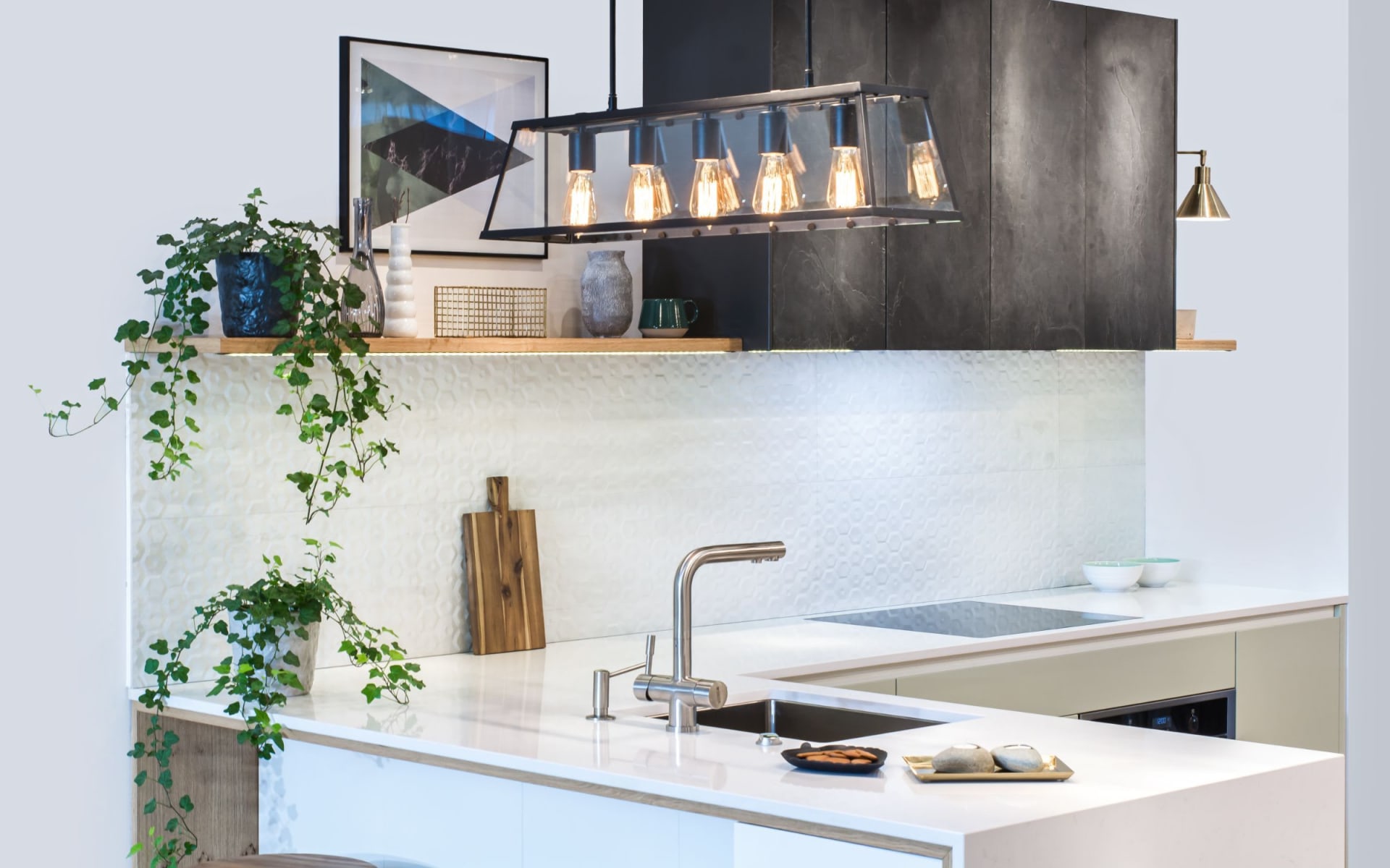 The image shows a modern kitchen with a large white island in the foreground featuring a stainless steel sink and faucet.
