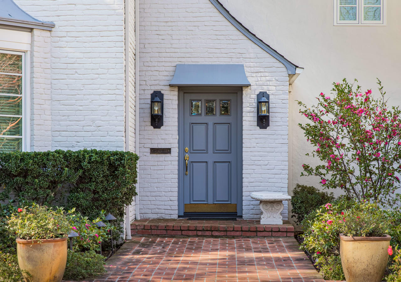 A welcoming white brick house with a bright blue door and a meandering brick walkway.