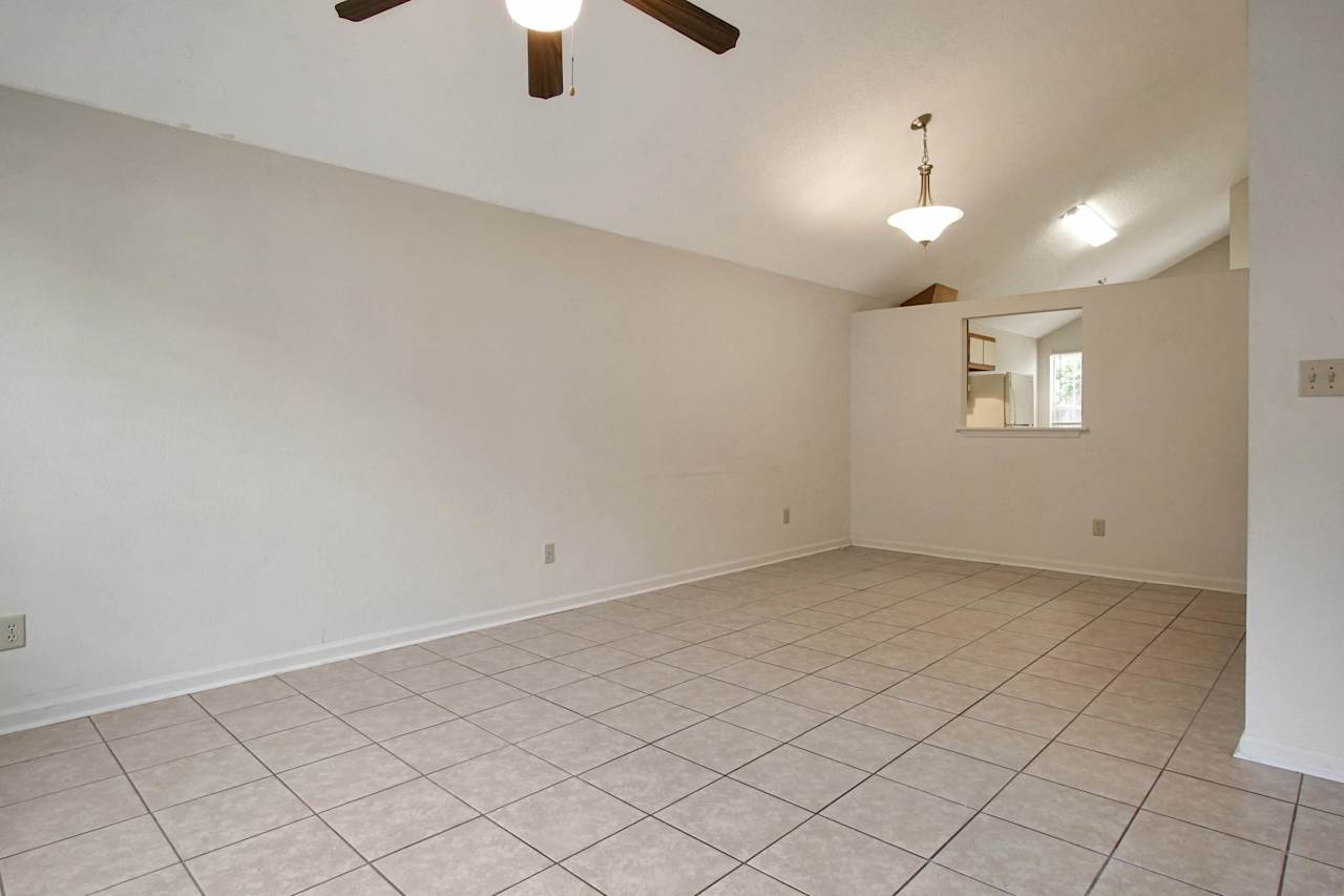 Photo of the main living area featuring white walls, lightly colored tile, vaulted ceilings, a ceiling fan with light fixture, a dining area with light fixture, and a pass through window into the kitchen  at 2709 Oak Park Court, Tallahassee, Florida 32308