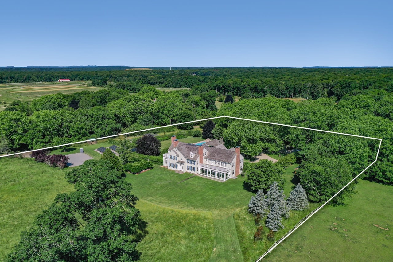 Large white multi-story house with a black roof, green lawn, and trees, located in Amagansett, NY.