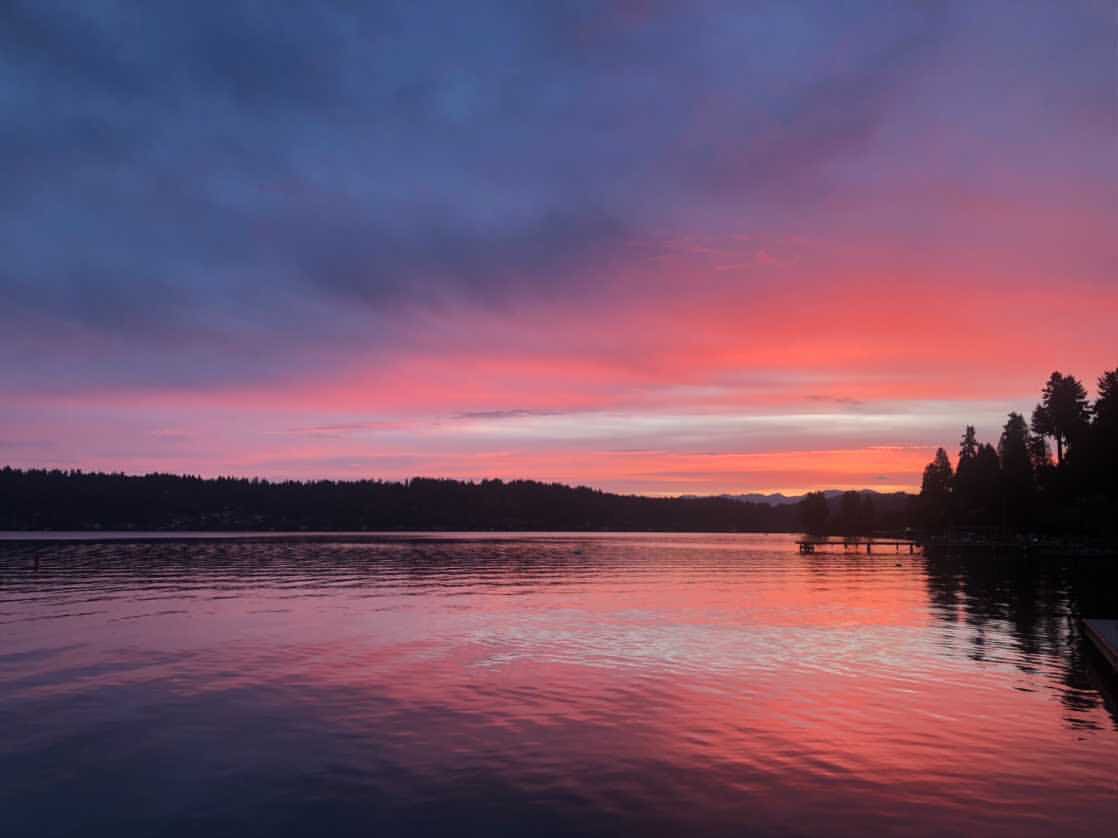 A pink and purple sunset over a lake with a dock in the foreground