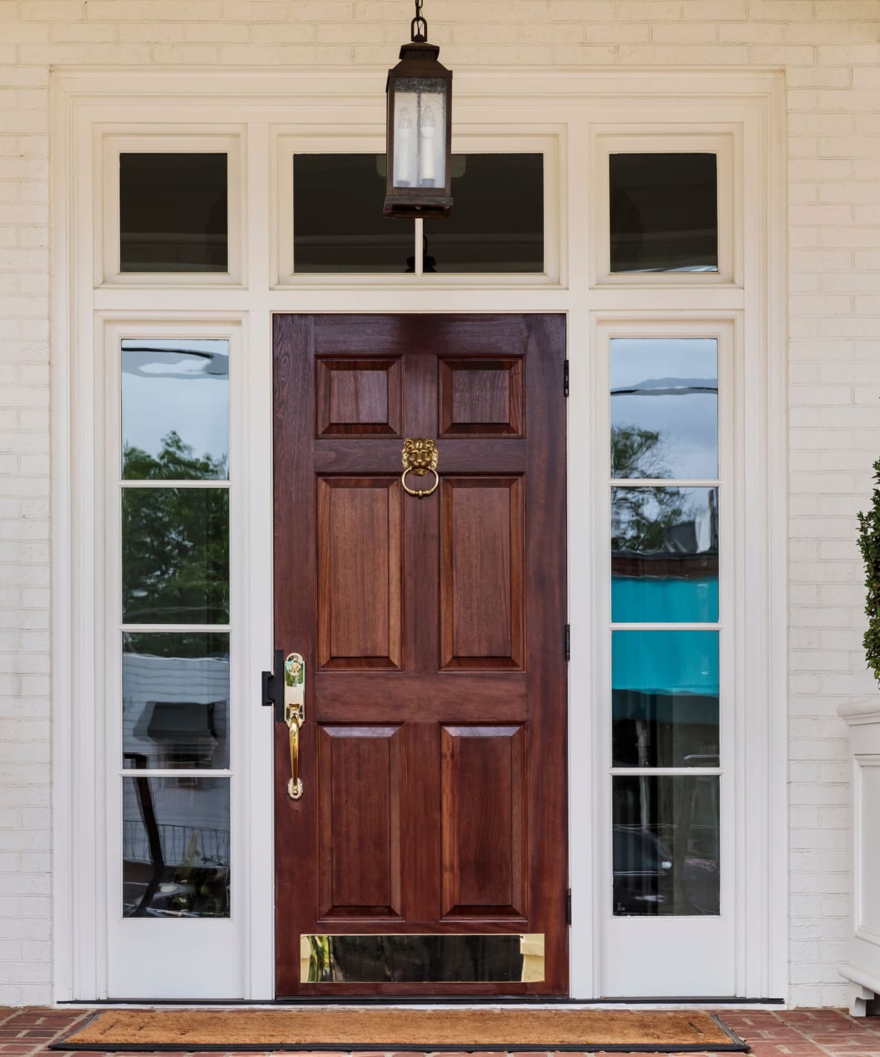 A brown wooden door with a brass lion door knocker and a black lantern hanging above it.