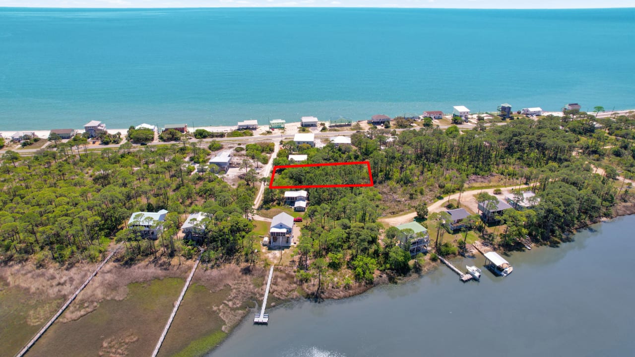 An aerial view image of a residential area, showing houses, yards, and a body of water in the background.