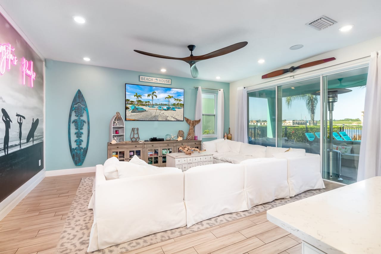 A living room in a beach house with a white couch, a television, and a sliding glass door.