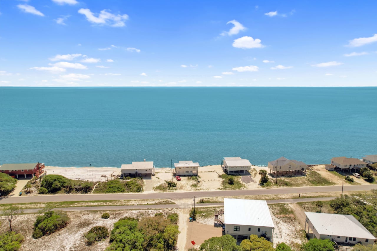 An aerial view of a coastal residential area with houses near the shoreline and the ocean in the background.