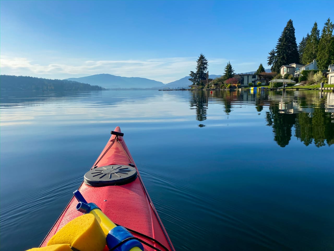 A red kayak floating on a calm lake, surrounded by trees and mountains