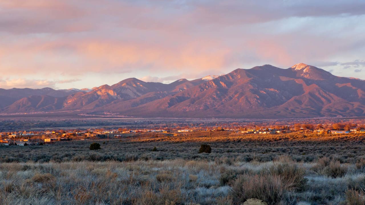 A sunset over a mountain range with a city in the distance.