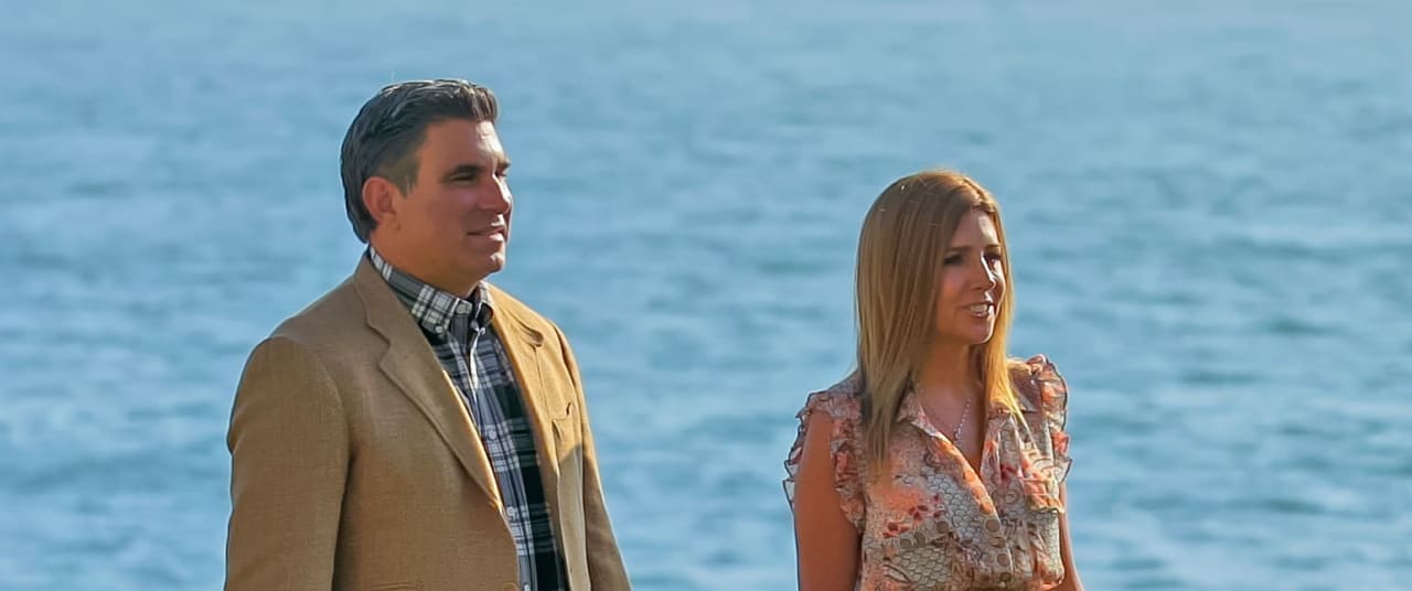 Danielle Donald and ​​​​​​​Ryan Clark standing in front of the ocean, dressed in casual but elegant attire.