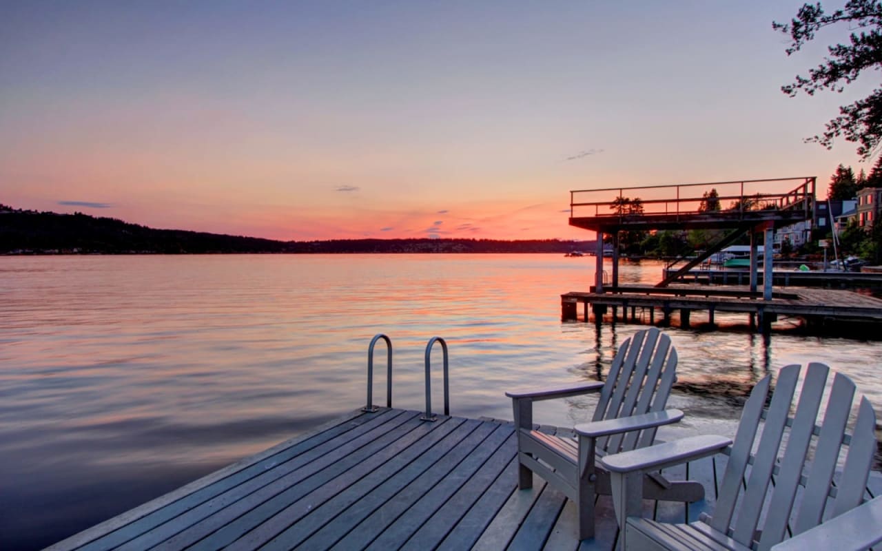 Two wooden chairs on a wooden dock over a lake at sunset