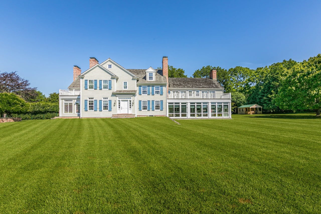 A spacious, white Georgian-style house surrounded by well-maintained lawns and trees.