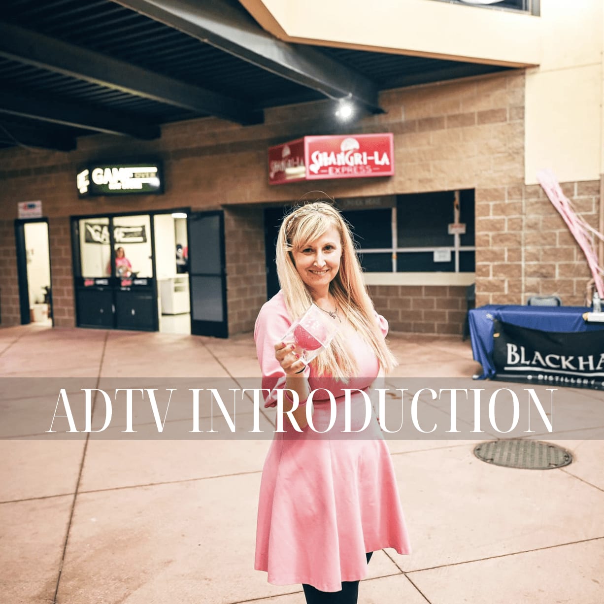 Smiling woman in a pink dress holding a glass, standing in front of a building. Text overlay reads 'ADTV INTRODUCTION.'