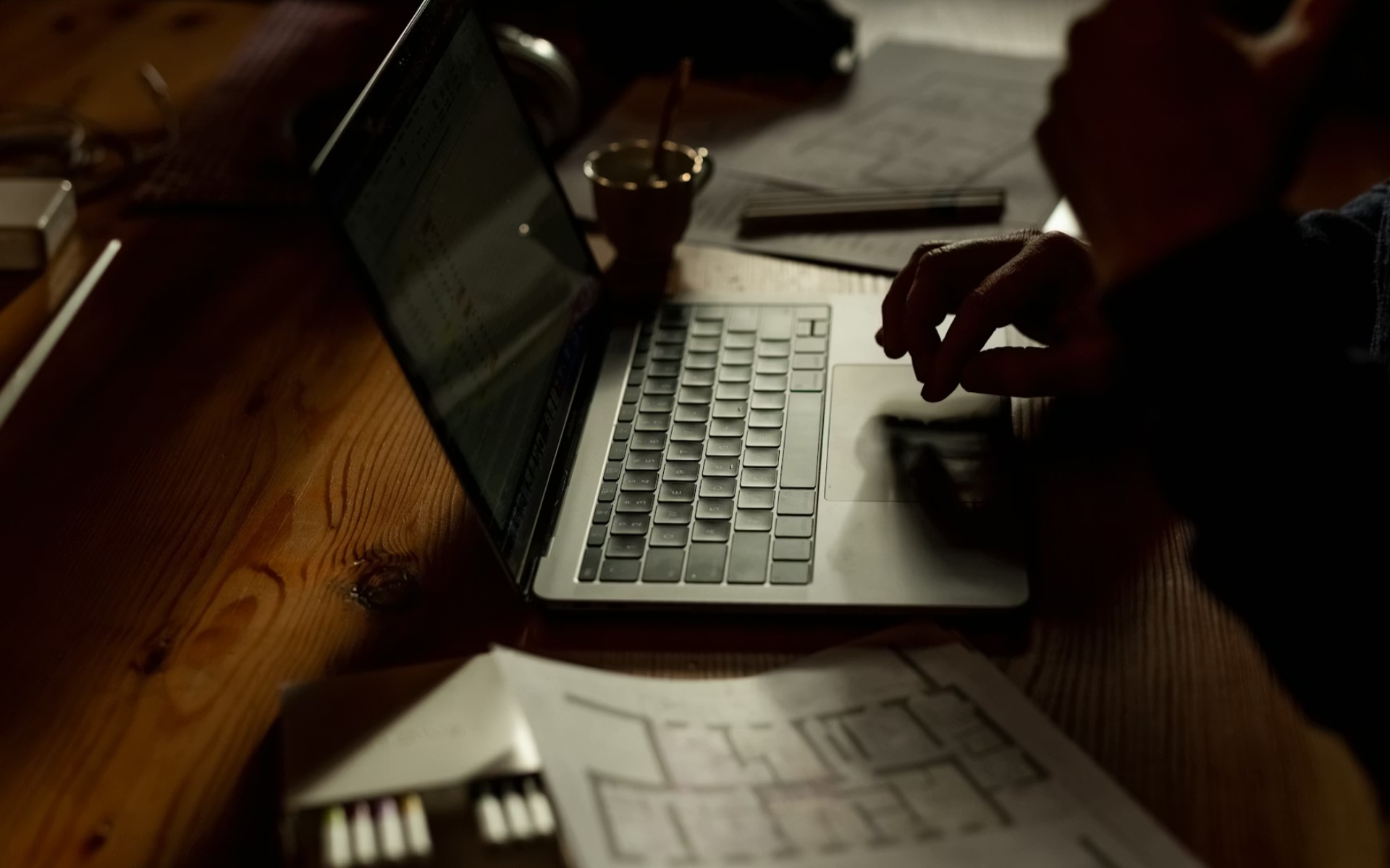 Person Browsing Real Estate Listings on Laptop with House Plans Nearby