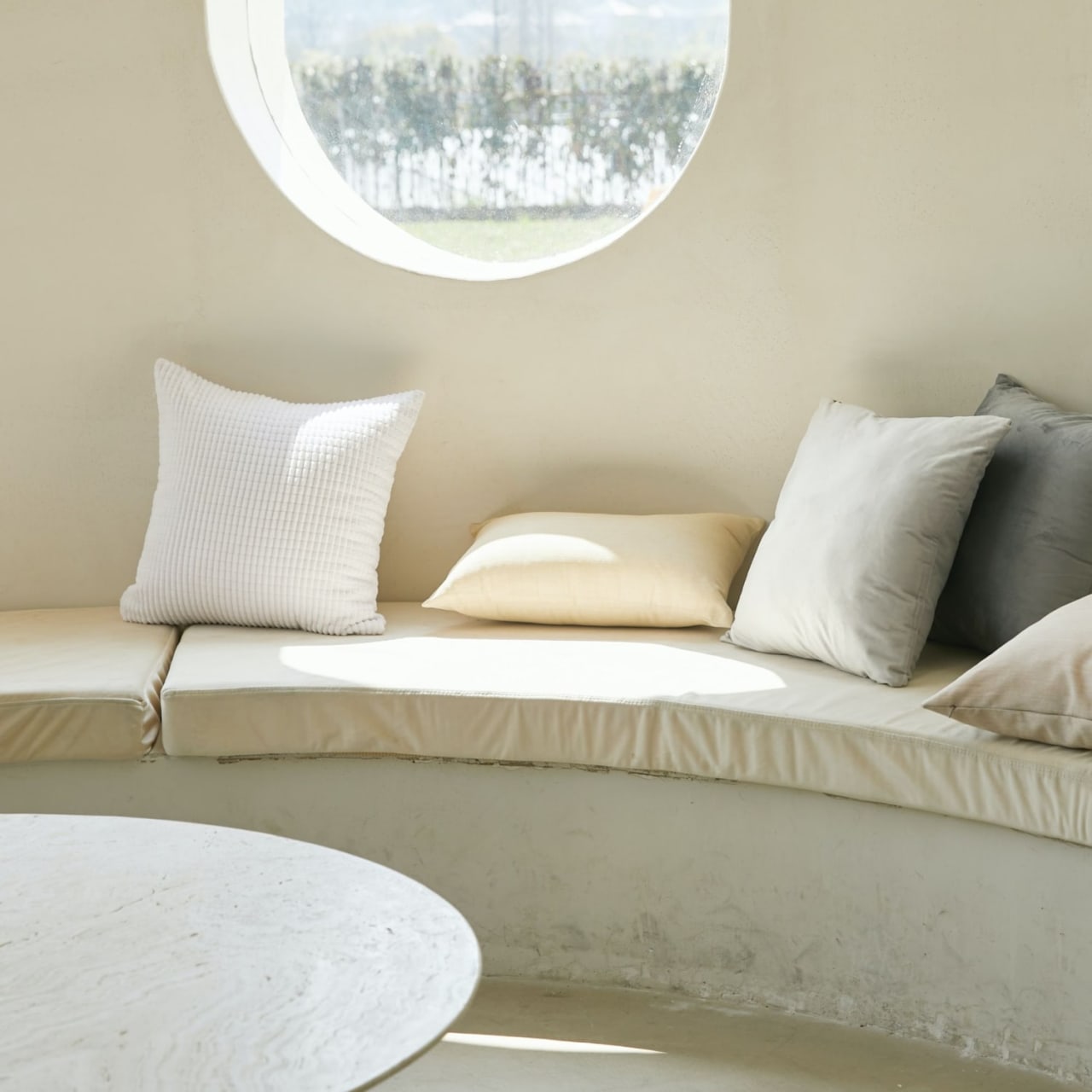 Couch with pillows in front of a round window overlooking a lush garden