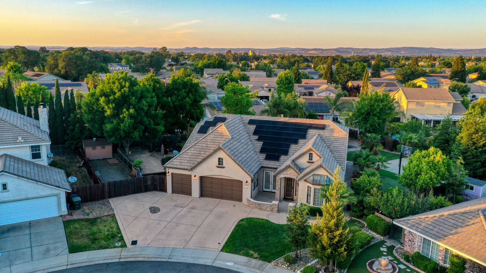 Golden-hour aerial of an established Rocklin, California neighborhood with mature trees and the Placer County foothills in the distance