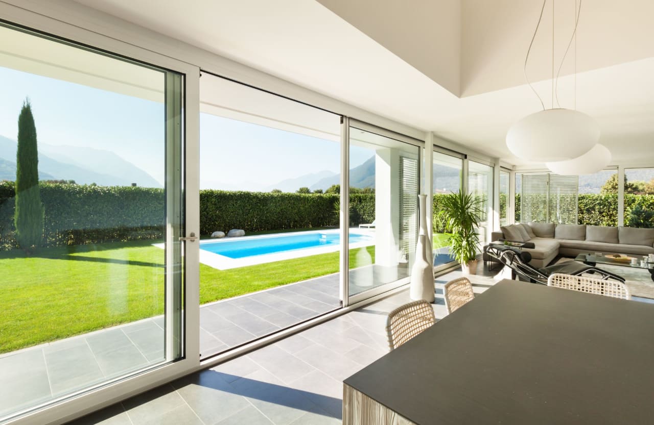 Modern living room with sliding glass doors leading to a backyard with a pool and lush greenery.