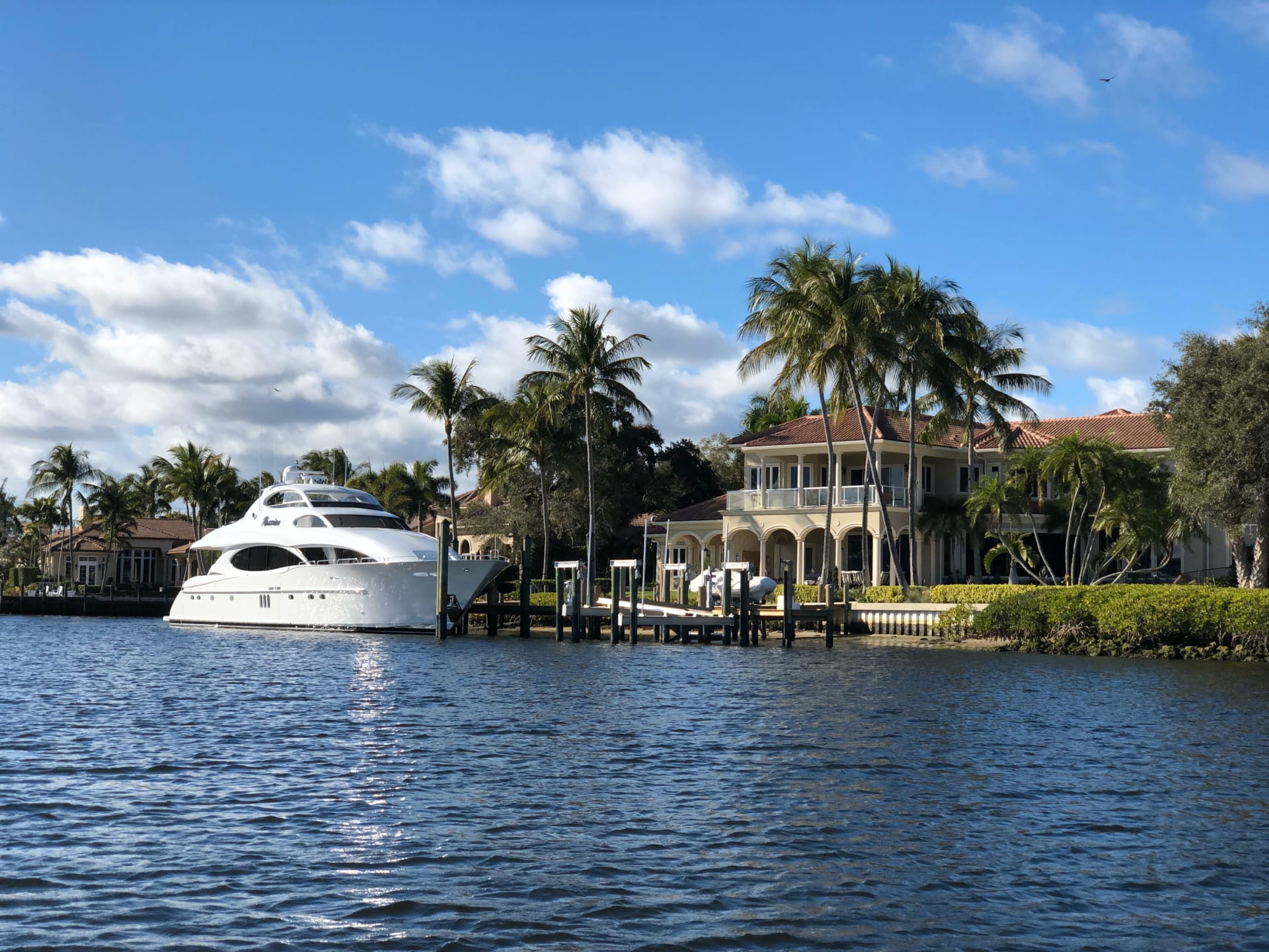 Waterfront home with palm trees, a private dock, and a white yacht moored offshore.
