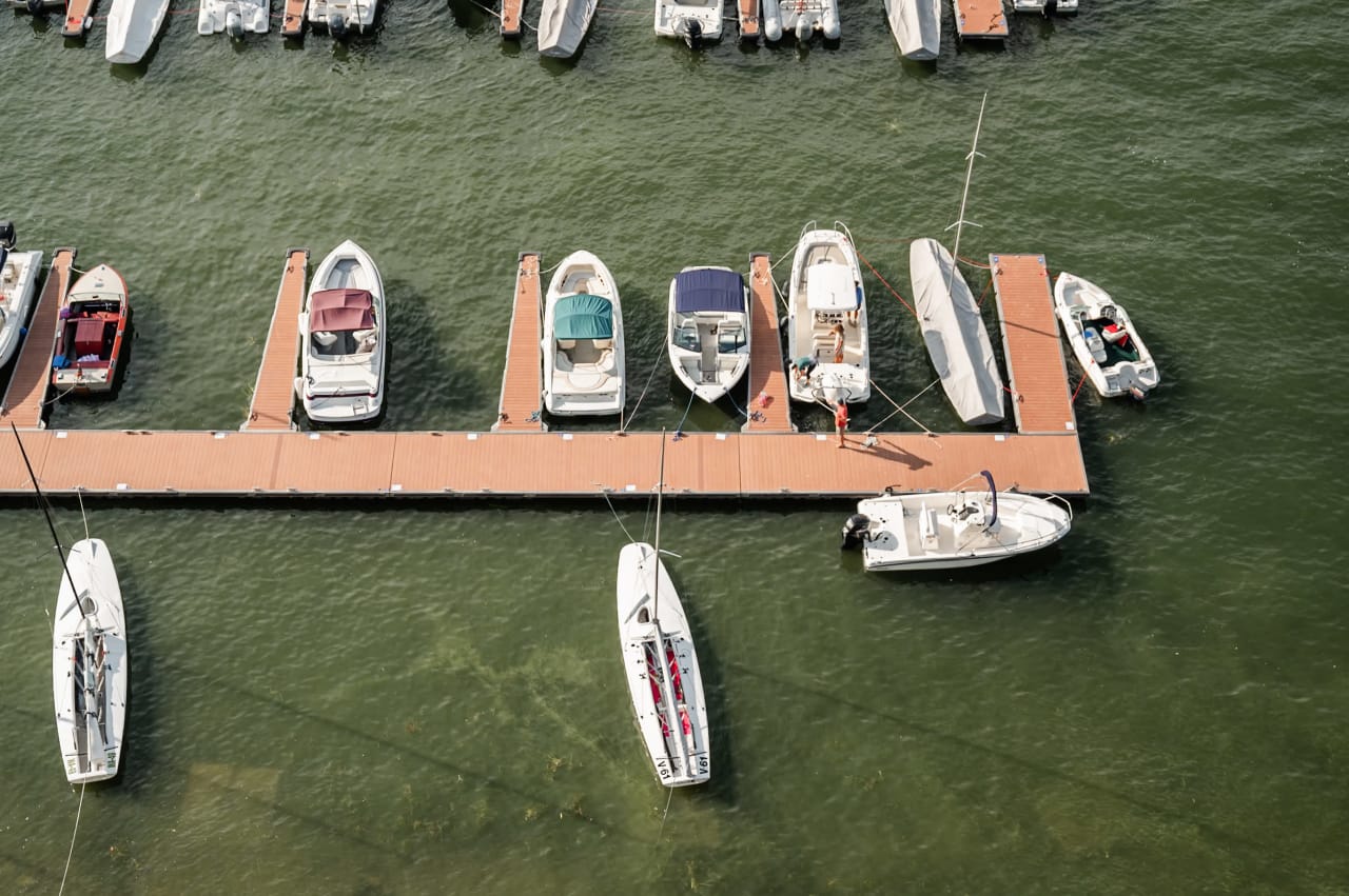 A top-down view of a marina with rows of sailboats and motorboats docked at floating piers.