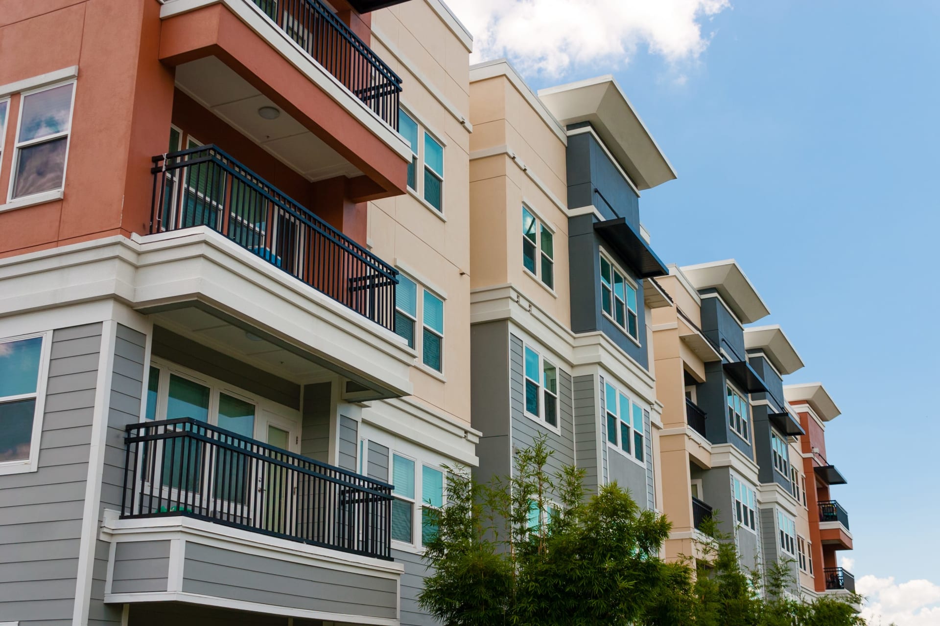 Modern multistory residences with colorful facades and black-railed balconies under a blue sky.
