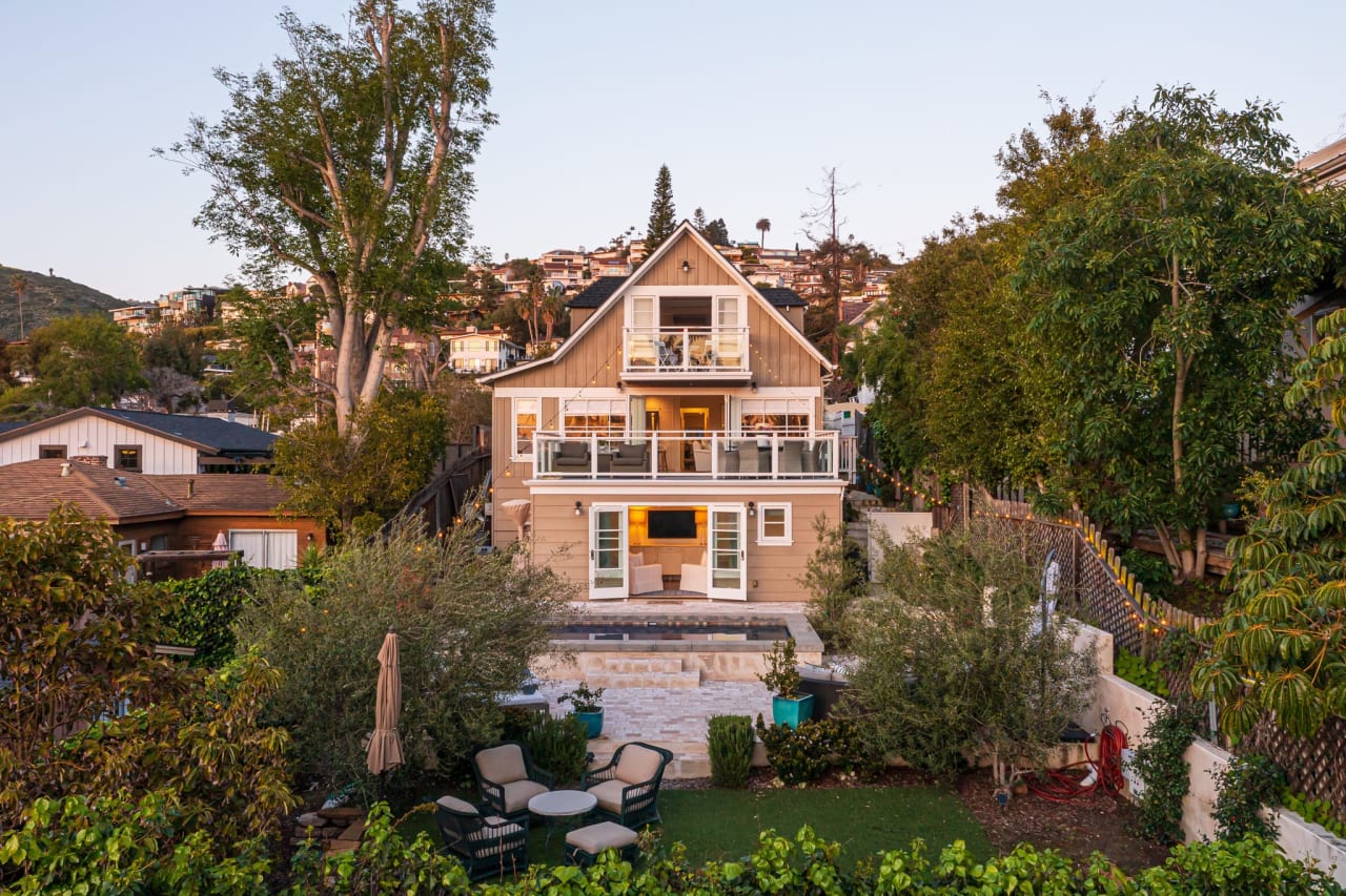 Back view of a three-story luxury home with large balconies and lush landscaping, located in a hillside neighborhood.