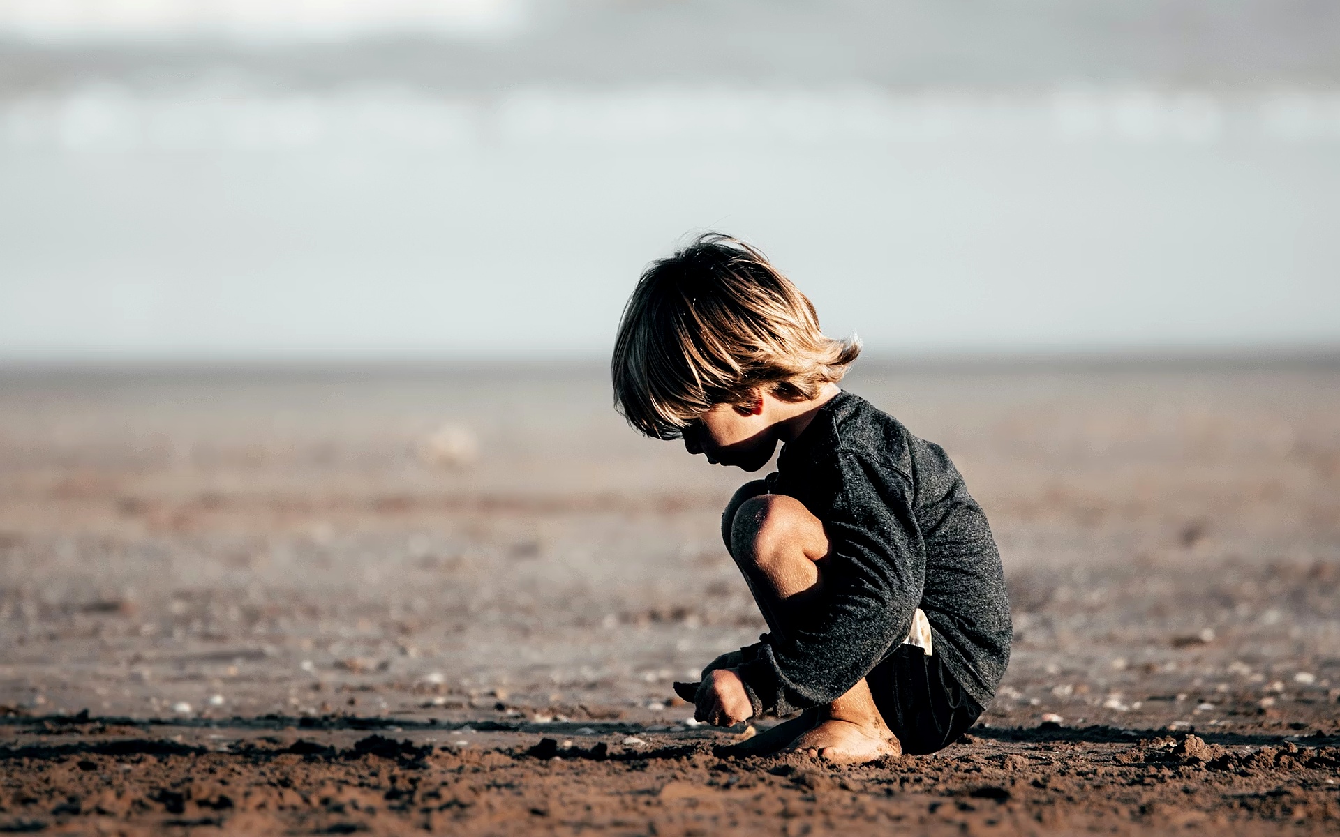 Young Child Squats On Beach Sand During Daytime