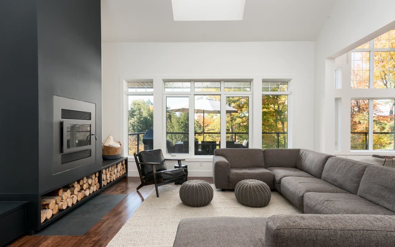 A modern living room with a large, black fireplace surrounded by a wood pile