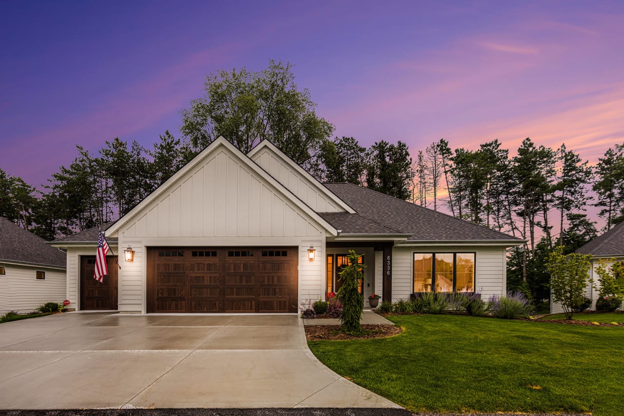 A white house with a brown garage door and a sunset in the background