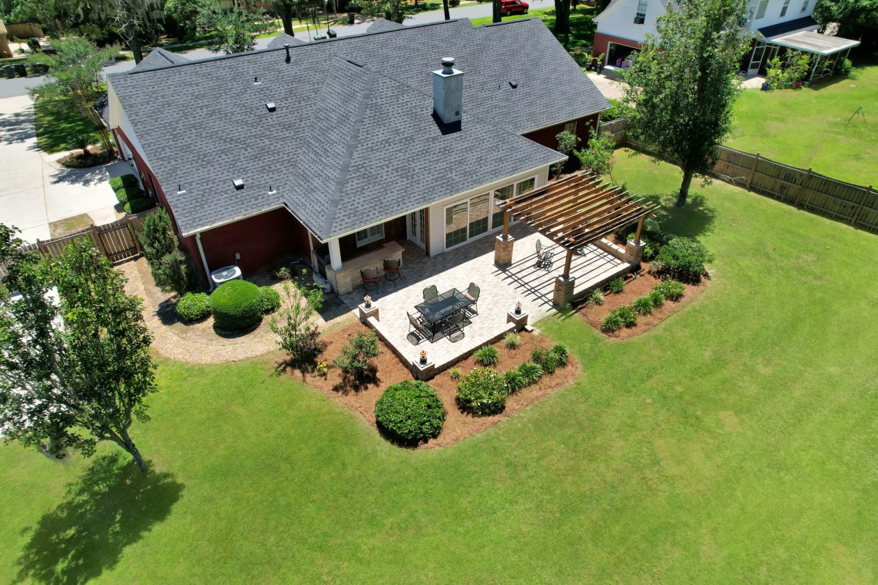 An aerial view of a house with a well-maintained lawn, landscaping, and outdoor seating area.